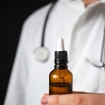 Doctor hands opening a glass pipette CBD oil bottle