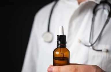 Doctor hands opening a glass pipette CBD oil bottle