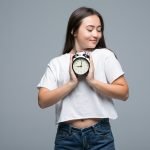Young Asian woman smile with a clock isolated on gray background