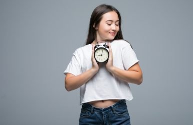 Young Asian woman smile with a clock isolated on gray background