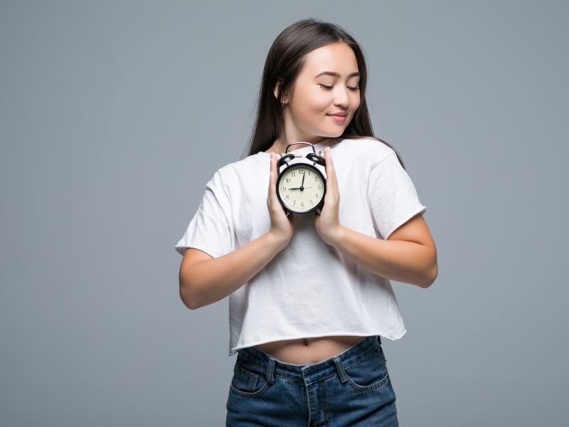 Young Asian woman smile with a clock isolated on gray background